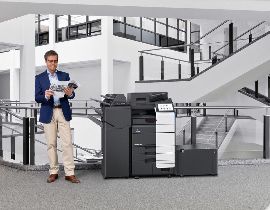 Cliente con un folleto junto a una impresora multifunción Konica Minolta en una oficina